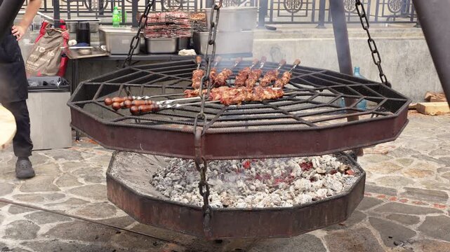 Chefs cook pilau and shish kebab outdoors in large kettles over open fire. Steam rising, charcoal grill, traditional cooking. Perfect for food, restaurant, or festival content.