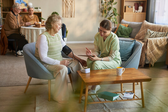 Senior woman receiving blood pressure check from young adult female nurse in nursing home, supporting elder care and health monitoring