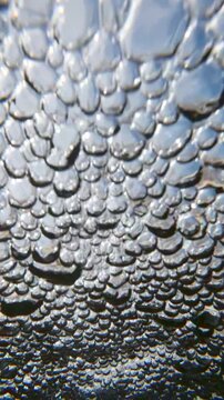 Slow motion: high-velocity rush of aerated water charging toward lens. Close-up of foaming bubbles of air as they sweep across surface in powerful, rapid-fire mountain stream. 