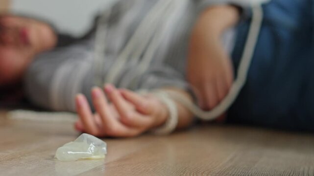 Close up of used condom falling next to tied-up female victim lying on wooden floor