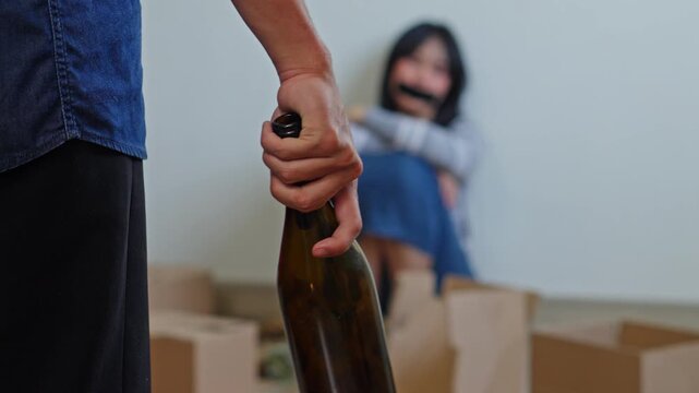Close up of hands kidnapper holding bottle with blurred captive woman in mouth taped at background
