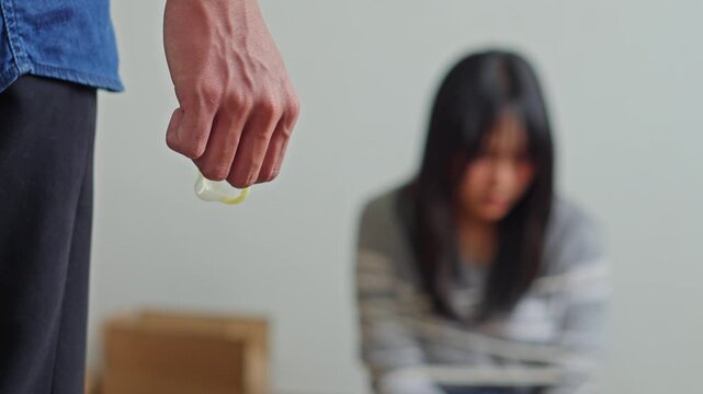 Close-up of trafficker hand holding condom with blurred victim tied up in background