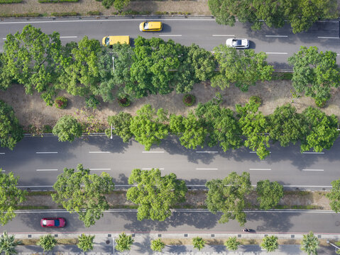 Aerial view of multi-lane city road with lush green trees and cars driving along the asphalt in Hsinchu, Hsinchu City, Taiwan.