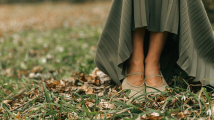 Woman's feet in ballet flats peeking out from under a flowing olive green pleated skirt