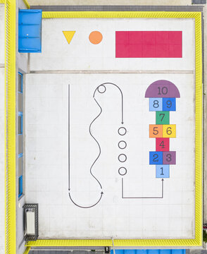 Aerial view of a colorful rooftop playground featuring a numbered hopscotch grid, geometric shapes, and a winding path enclosed by a bright yellow fence Taiwan.