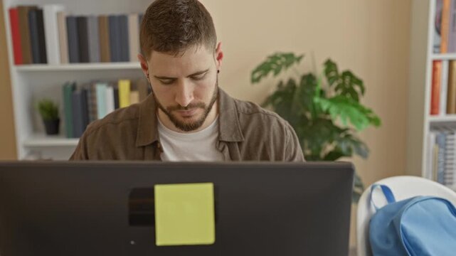 Man peels and eats a banana at a desktop computer desk in a building, reaching into a blue backpack beside him while seated; concentration break.