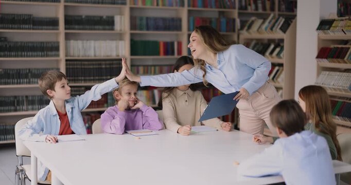 Teacher gives high five to schoolboy, encouraging active participation during class. Friendly relations between educator and schoolkid, student motivation, supportive teaching primary school education