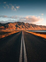 Naklejka premium Long road stretching towards golden mountain range and lake Sunset sky with pink clouds and scenic natural landscape