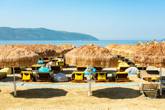 vibrant Balkans beach scene filled with people relaxing under umbrellas along turquoise coastline, Tourists enjoy sun and sea, Albania vacation, Natural beauty meets human activity