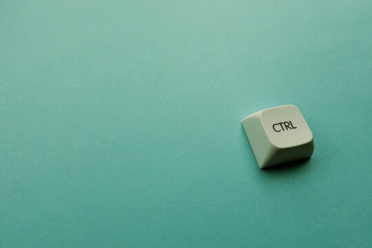 A white CTRL keyboard keycap on a teal surface. This isolated component symbolizes the fragmentation of command structures and the paradox of autonomy in standardized technological systems.