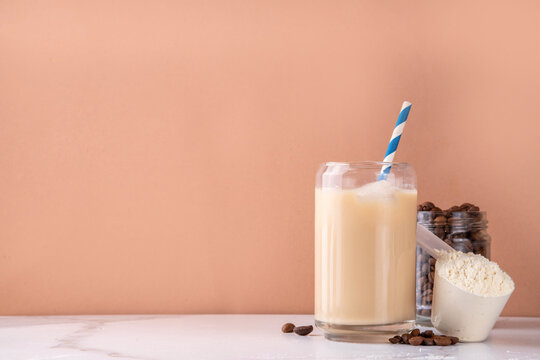 Iced protein coffee, whey isolate latte drink with whey protein powder in scoop and coffee beans, on kitchen table copy space