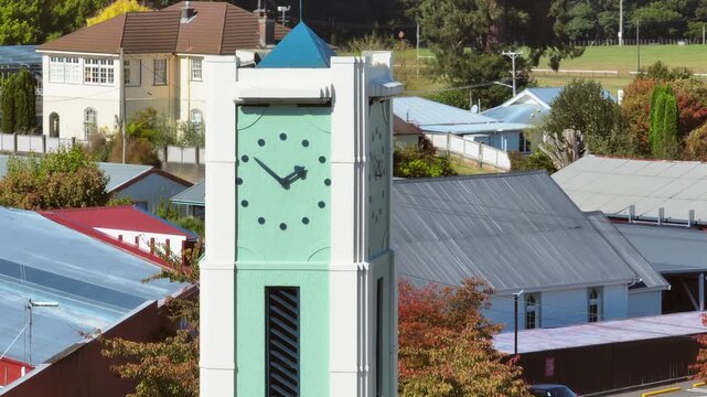 A clock tower stands tall in Taihape, Manawatu-Whanganui, New Zealand, with buildings and trees surrounding it. The clock shows it is almost 10 o'clock.