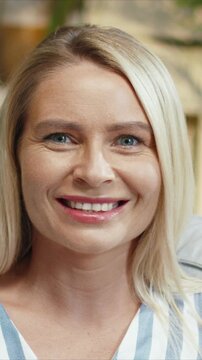 Close portrait of beautiful Caucasian woman looking at camera and smiling. Female showing calm expression and clear eyes. Holding steady gaze and relaxing. Sitting at home in light room.
