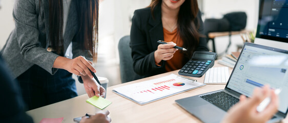 Business team analyzing financial data on laptops and charts, with a hand pointing to note in...