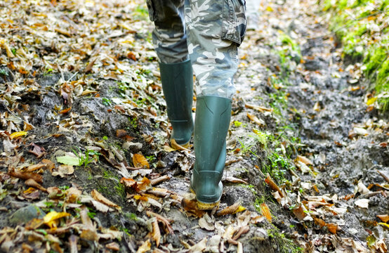 Man in Rubber Boots Walking on Muddy Forest Path, low angle rear view. Concept of hiking, hunting, or outdoor work