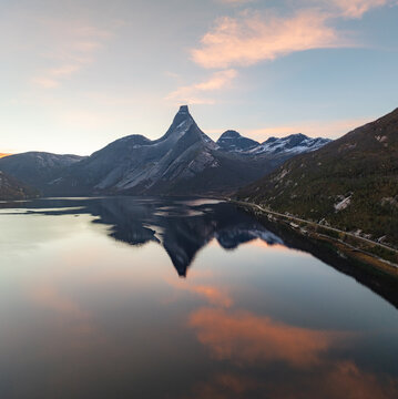 Aerial view of the iconic Stetind mountain peak reflecting in the calm waters of a fjord under a sunset sky in Narvik Municipality, Nordland, Norway.