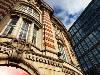 Naklejka premium Historic stone and brick building facade in Manchester UK with ornate columns and contrast against modern glass tower and blue sky