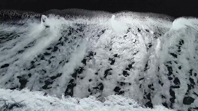 Dynamic video captures powerful ocean waves breaking with foamy white water on a dark, rugged shoreline. Experience the raw, mesmerizing energy of the sea's relentless motion
