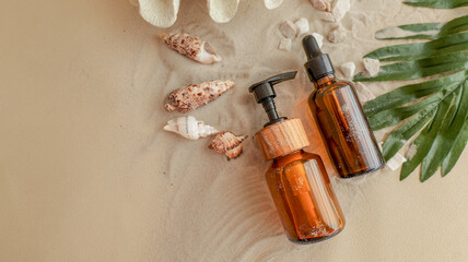 Obraz premium Elegant amber bottles on sandy beach with seashells and green leaves