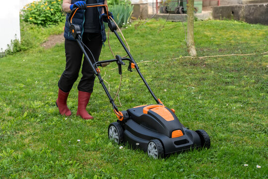 Middle aged woman houseowner mowing the lawn on backyard of his house.