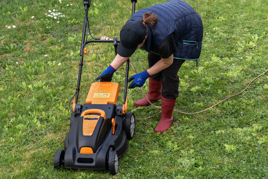Middle aged woman houseowner mowing the lawn on backyard of his house.