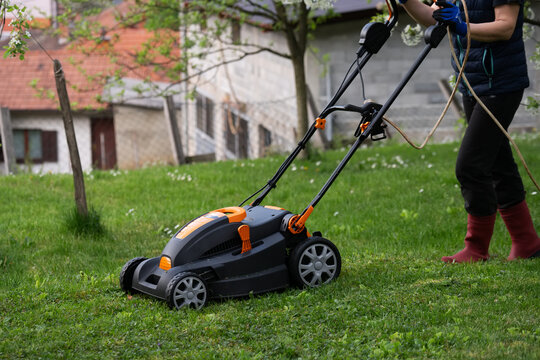 Middle aged woman houseowner mowing the lawn on backyard of his house.