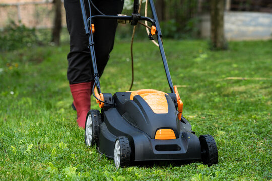 Middle aged woman houseowner mowing the lawn on backyard of his house.