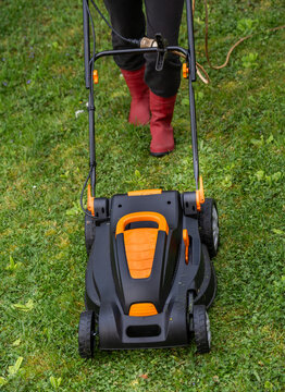 Middle aged woman houseowner mowing the lawn on backyard of his house.