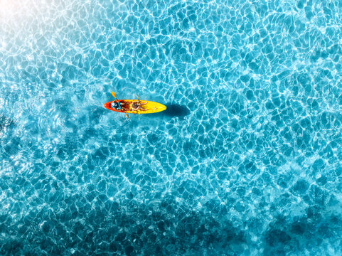 Aerial drone view of a kayakers paddling through vibrant turquoise shallow water in deep blue sea in summer. Mallorca, Spain. Balearic Islands. Tropical paradise. Top down view of canoe. Travel
