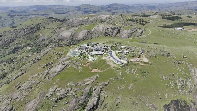 Drone orbits to left in ultra wide shot high above north side of resort on a sunny day at Sibebe Rock near Mbabane, Eswatini