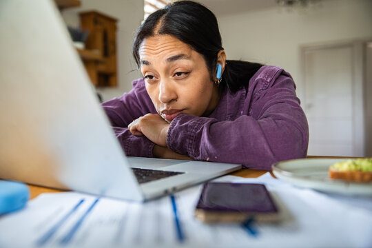 Tired woman with earbuds working on laptop at home