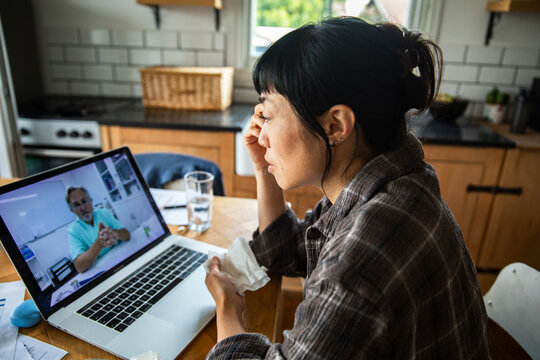 Sick woman consulting doctor via video call in home kitchen