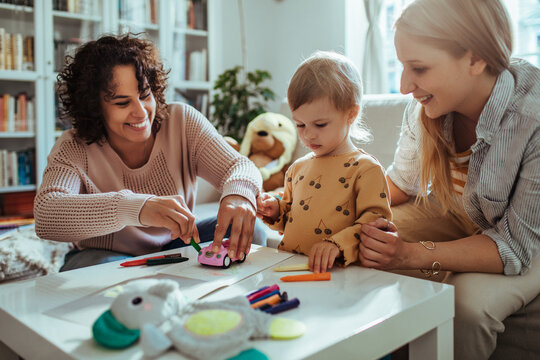 Two women helping toddler with arts and crafts at home