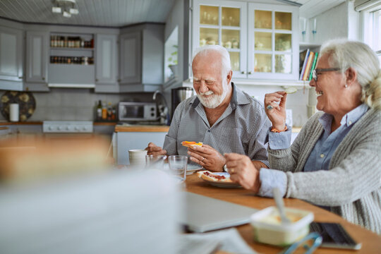 Happy senior couple eating breakfast in home kitchen