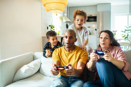 Parents and kids playing video games on sofa at home