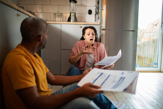 Stressed couple reviewing bills on kitchen floor at home