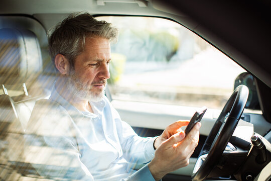 Middle-aged man using smartphone in parked car