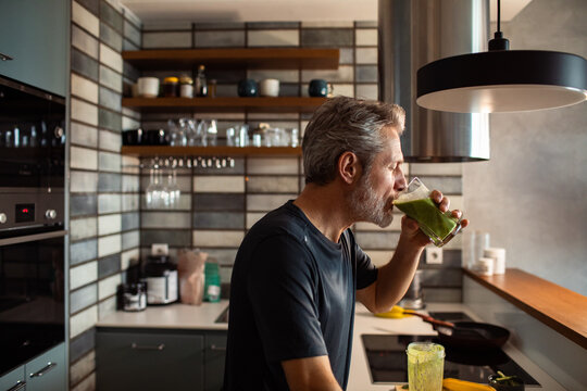 Middle-aged man drinking green smoothie in modern home kitchen