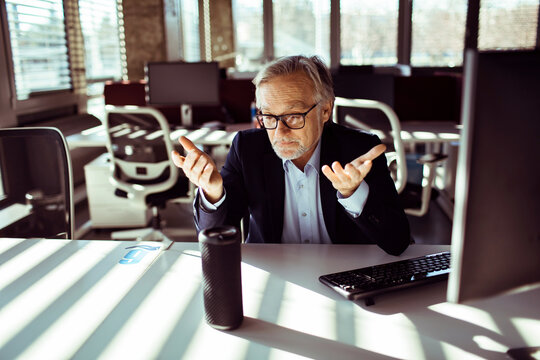 Mature businessman gesturing at smart speaker in office