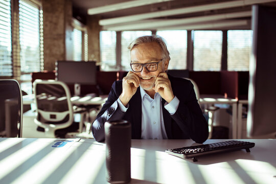 Smiling senior businessman using smart speaker in modern office