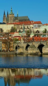 Experience the captivating beauty of Pragues architecture and reflections in the river. Charming rooftops and iconic landmarks highlight the citys allure during a sunny day.