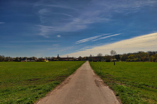 Gerader Feldweg f&uuml;hrt zur Silhouette des Dorfes Kollenbey, weite Wiesenlandschaft mit dramatischem Wolkenhimmel in der Saale-Elster-Aue, Kollenbey, Schkopau, Saalekreis, Sachsen-Anhalt, Deutschland