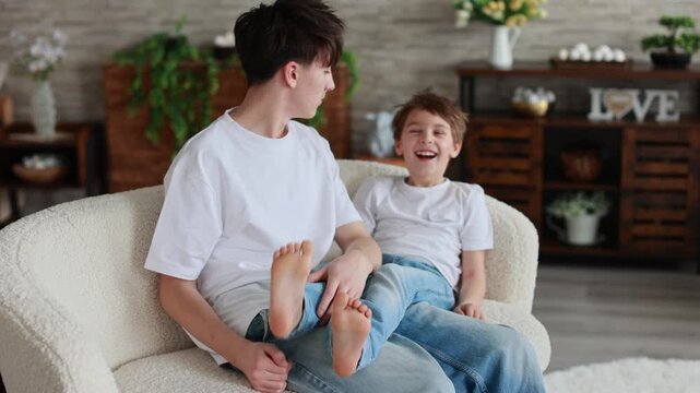 Happy positive children, tickling on the feet, having fun together, boy brothers at home having wonderful day with joy