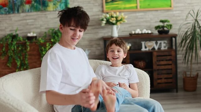 Happy positive children, tickling on the feet, having fun together, boy brothers at home having wonderful day with joy