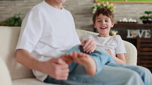 Happy positive children, tickling on the feet, having fun together, boy brothers at home having wonderful day with joy
