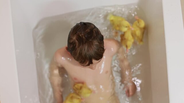 Cute little blond boy, playing with little ducklings in the bathtub at home, happiness. Child and animal interacting together