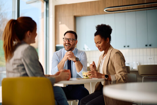 Happy businessman laughing while talking to female colleagues on lunch break at work.