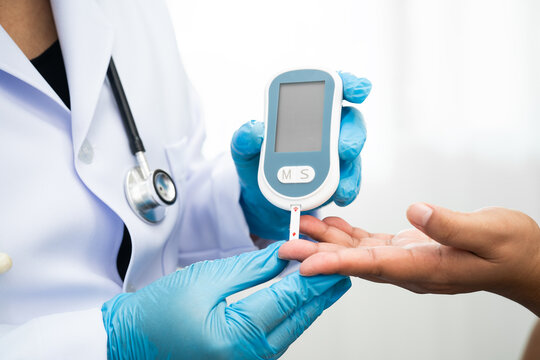 Asian doctor using digital glucose meter for check sample blood sugar level to treatment diabetes.