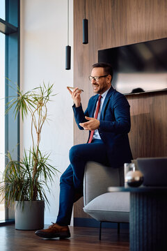 Happy businessman talking over cell phone's speakerphone in office.