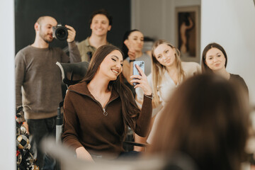 Fototapeta premium A young woman takes a mirror selfie in a beauty center while friends and a photographer look on. She smiles in a salon chair as her friends pose behind her.